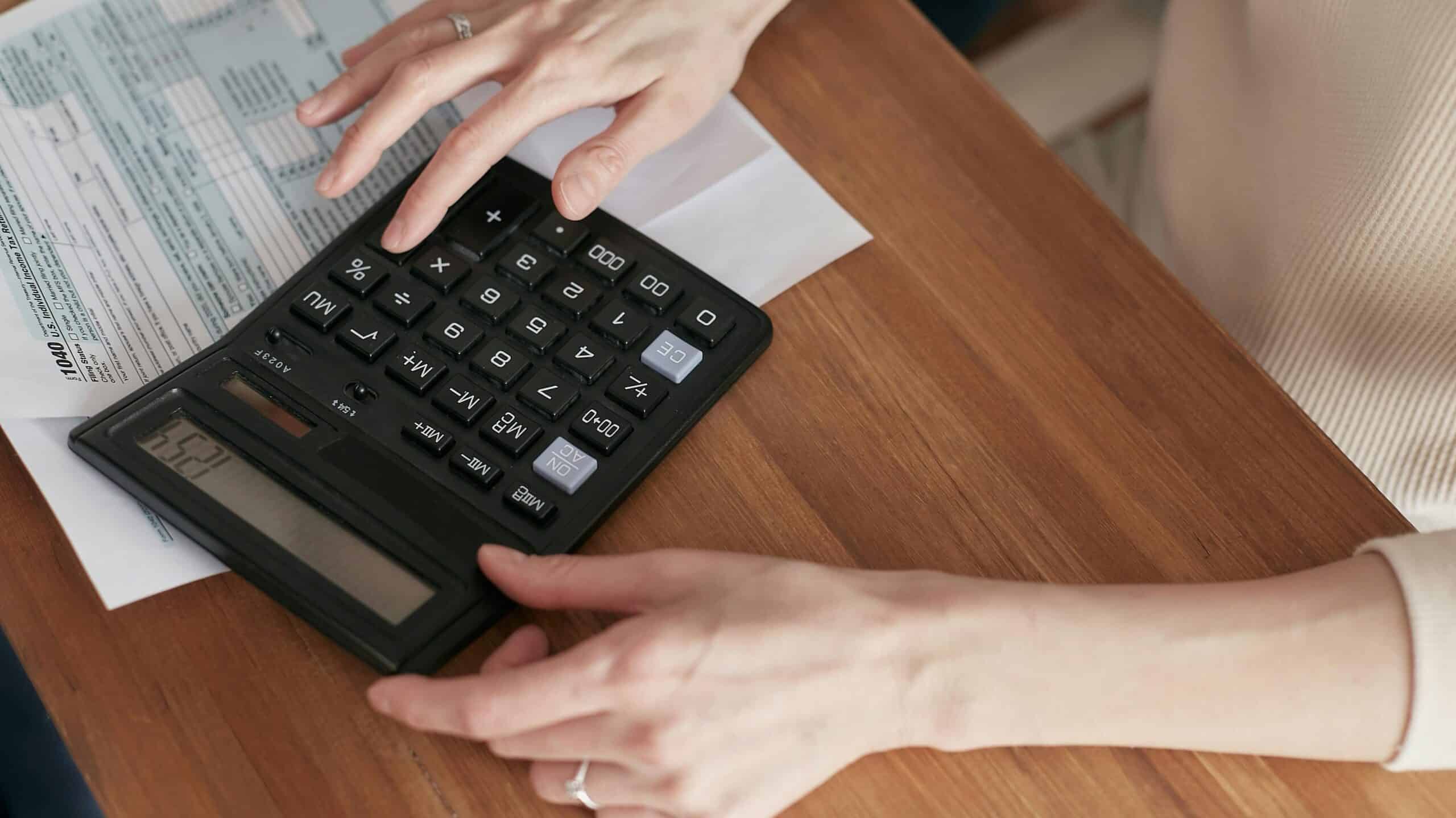 Hands using a large calculator on a wooden table with financial documents for budgeting a DIY project