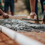How to Choose the Best Foundation for Clay Soil Workers leveling wet concrete for a new foundation on clay soil during home construction.c