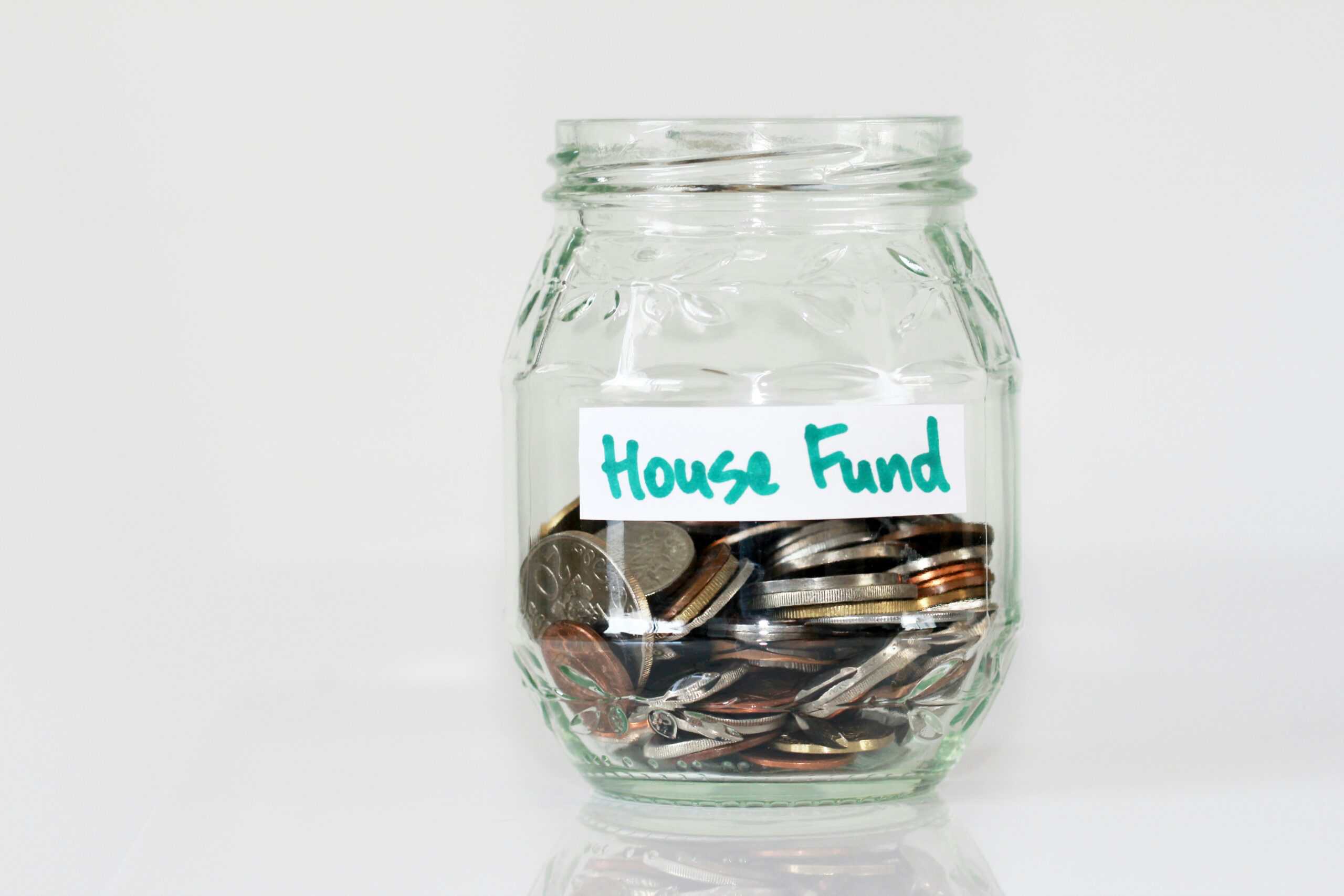 Glass jar labeled house fund filled with coins representing budgeting for a DIY basement finishing project