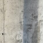 Damp concrete basement wall showing moisture staining and discoloration, indicating walls are not ready for painting